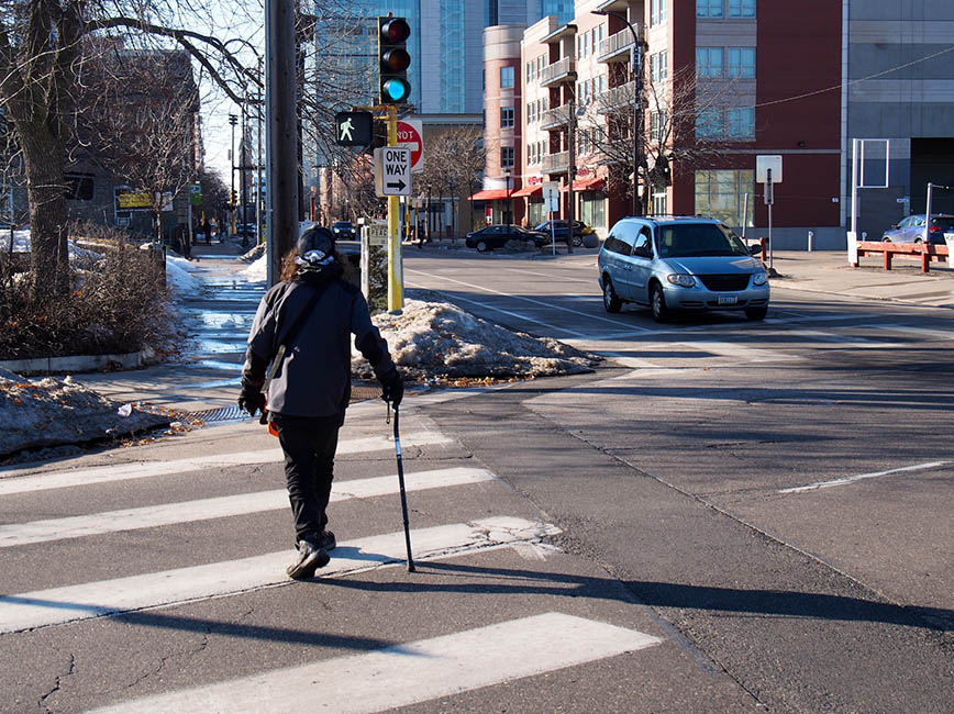 A person with a walking stick crossing the street