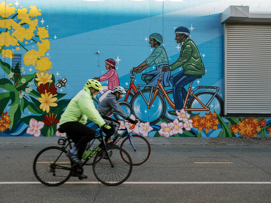 Two bicyclists riding in front of a mural