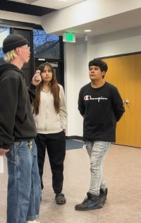 Person interviewing two students in a school with a handheld microphone.