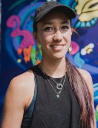 Artist Myers wearing a hat and jewelry in front of a brightly colored abstract image