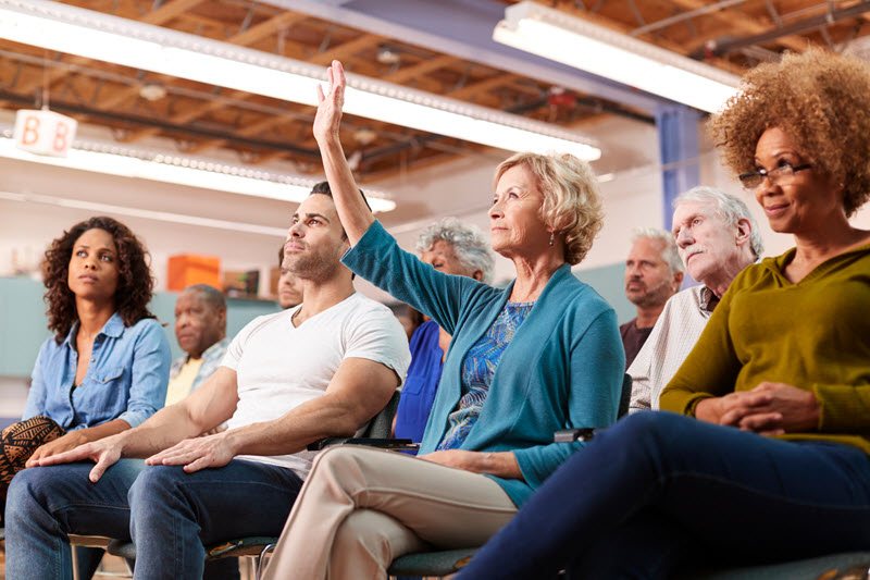 Woman seated in a meeting raising her hand