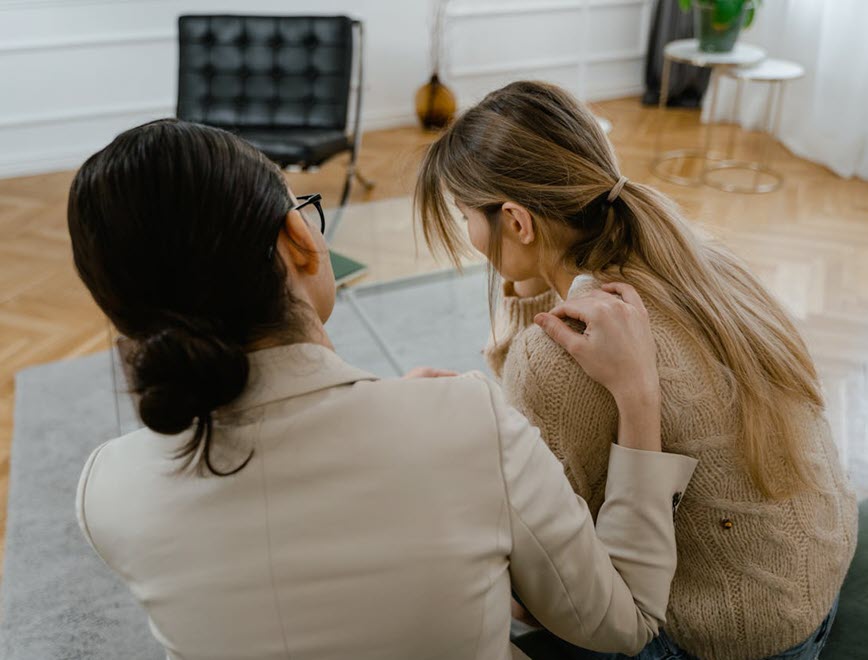 A person with a comforting hand on another while sitting on a bench.