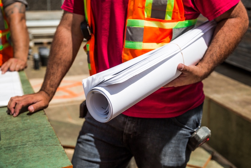 Person in orange and yellow vest holding blueprints