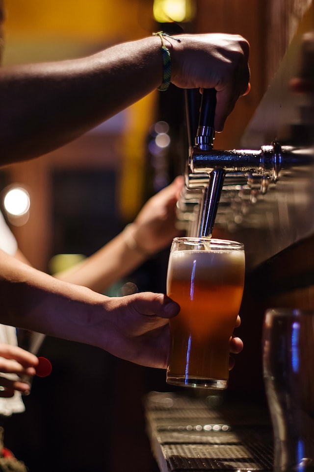 person putting beer in glass from tap